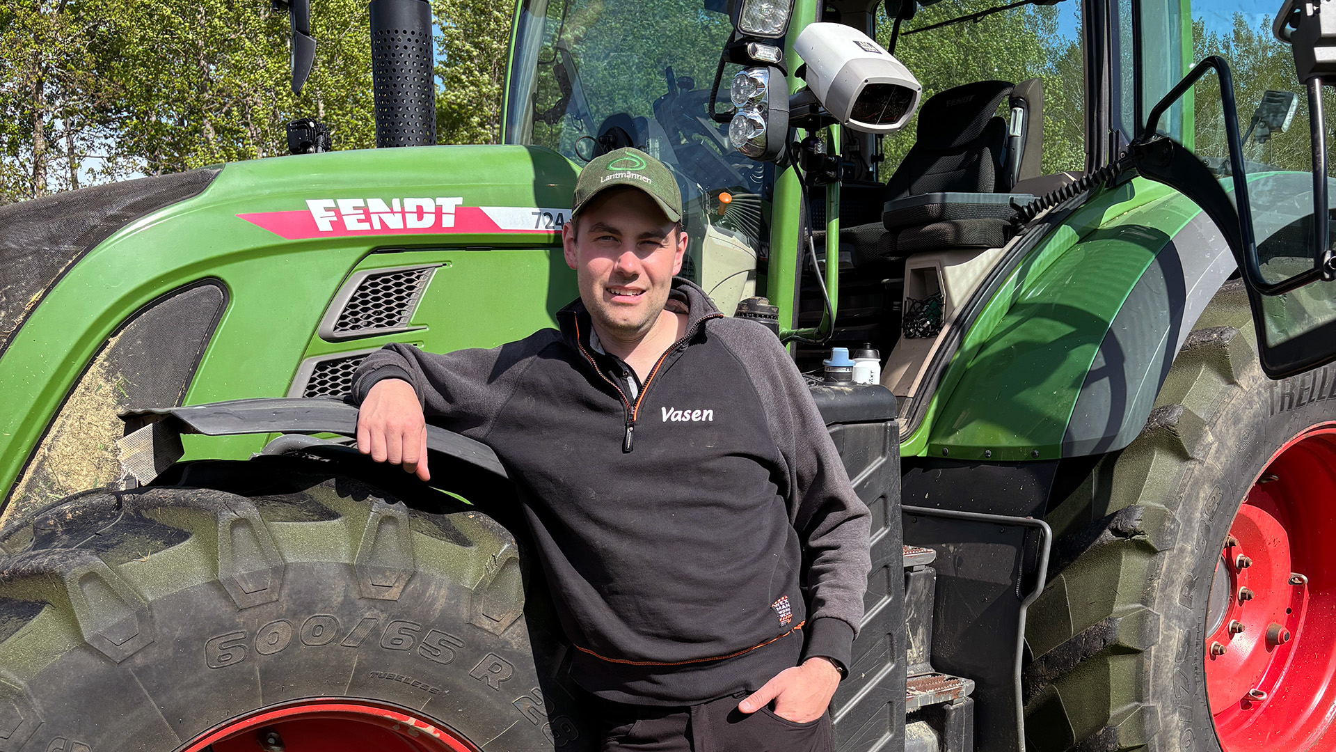 En man st&aring;r och h&auml;nger p&aring; ett d&auml;ck framf&ouml;r en gr&ouml;n traktor.